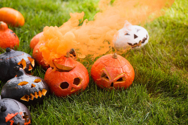 carved and spooky pumpkins with orange smoke on green lawn - Foto, afbeelding
