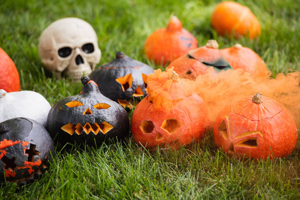 carved pumpkins with orange smoke near blurred skull on green lawn - Foto, Bild