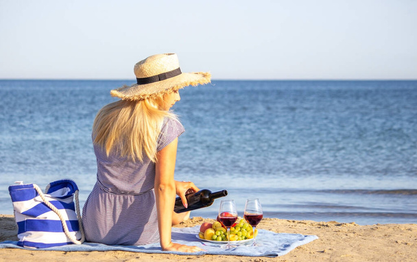 Hermosa mujer sonriente con una copa de vino en la playa. Vino tinto de frutas. Enfoque selectivo. - Foto, Imagen