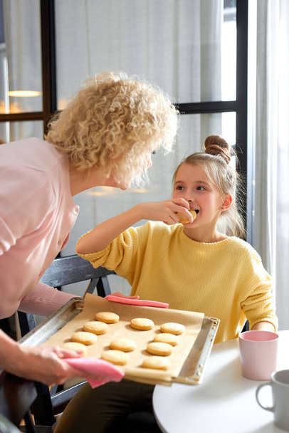 Senior granny came with prepared cooked cookies, child girl is tasting it - Fotografie, Obrázek