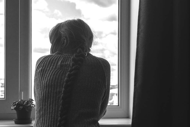 Szomorú fiatal nő sziluett az ablakpárkányon háttér, másolás tér  - Fotó, kép