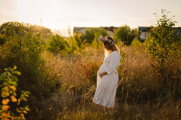 Hamile bir kadının portresi. Beyaz elbiseli güzel hamile bir kadın tarlada yürüyor.. - Fotoğraf, Görsel
