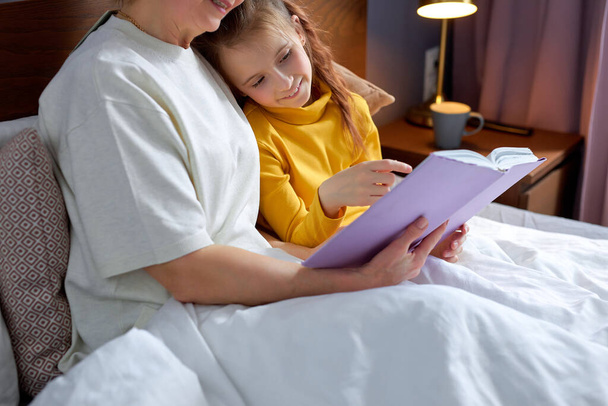 Nice Grandmother reading tales to daughter before laying down to sleep - Fotoğraf, Görsel