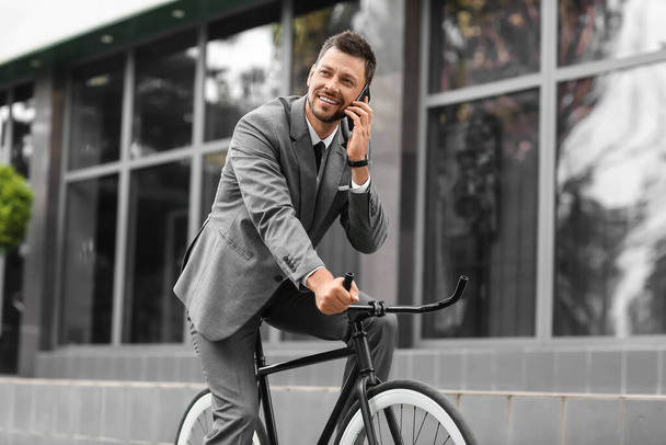 Businessman with mobile phone riding bicycle on city street - Photo, Image