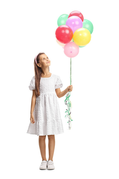 Full length portrait of a girl in a white dress holding a bunch of balloons and looking up isolated on white background - Photo, image