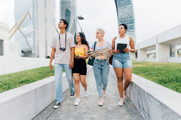Grupo de jovens amigos multiétnicos turistas caminhando passeios usando mapa e procurando informações com tablet e smartphone rindo - Foto, Imagem