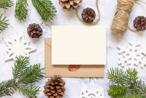 Winter Christmas Composition with a card over sealed envelope flat lay. Christmas and New Year greeting card template with fir tree branches, pine cones, snowflakes and rope on marble background top view. Holiday mockup. - Photo, Image