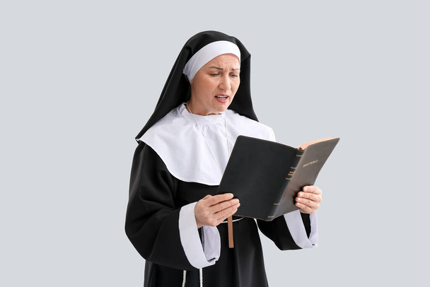 Mature nun reading Holy Bible on light background - Foto, afbeelding