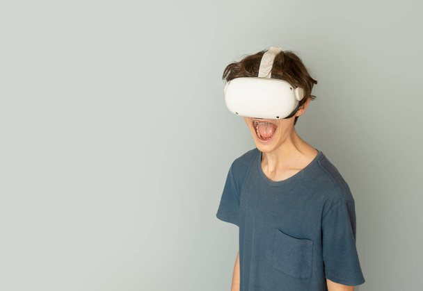 adolescente niño jugando realidad virtual sobre fondo gris, concepto de tecnología digital, tecnologías innovadoras - Foto, Imagen