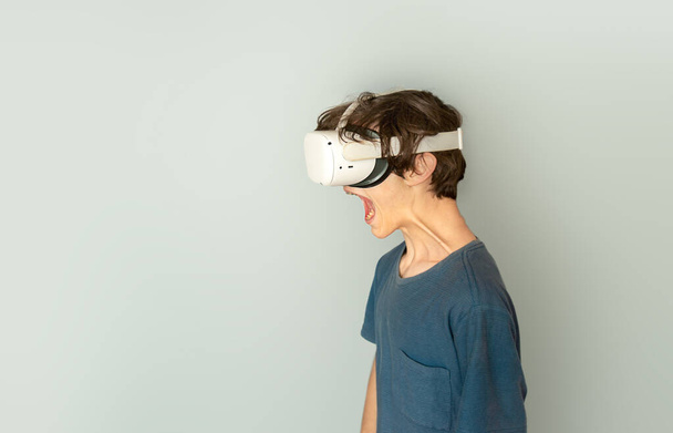 мальчик-подросток, играющий в виртуальную реальность на сером фоне, концепция цифровых технологий, инновационные технологии - Фото, изображение