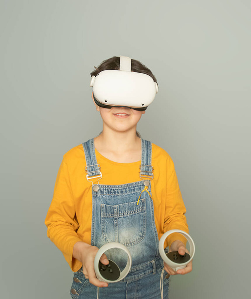 Niña jugando realidad virtual sobre fondo gris, concepto de tecnología digital, tecnologías innovadoras - Foto, imagen