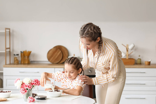 Little girl and her mother having breakfast in kitchen - Фото, изображение