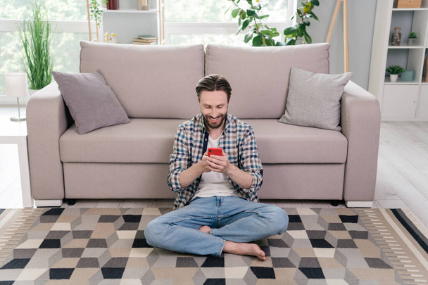Portrait of attractive focused cheerful guy sitting on carpet using device smm app 5g staying home at light room indoors - Photo, Image