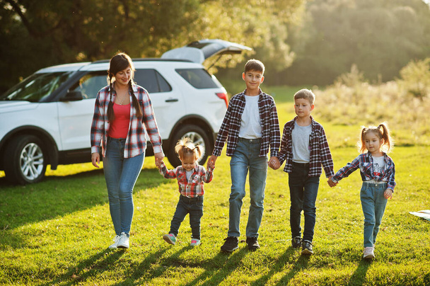 Family spending time together. Mother with four kids standing and holding hands against white suv car. - Foto, imagen