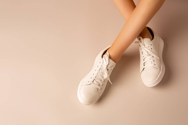 Nenáročná obuv - bílé kožené tenisky boty a dívky zkřížené nohy na nahé pozadí. Rozvržení s volným místem pro kopie. - Fotografie, Obrázek