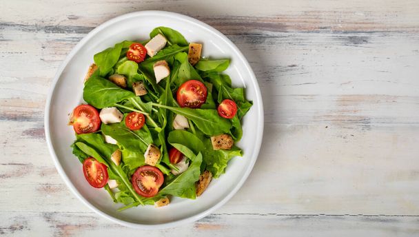 Fresh spinach salad with tomato, small pieces of herb roasted chicken in white ceramic dish on white wooded table. Concept for healthy. Studio picture. - Photo, Image