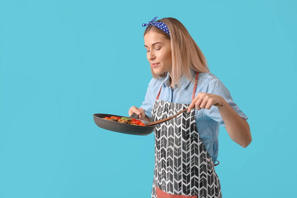 Mladá hospodyňka s chutným pokrmem v pánvi na barevném pozadí - Fotografie, Obrázek