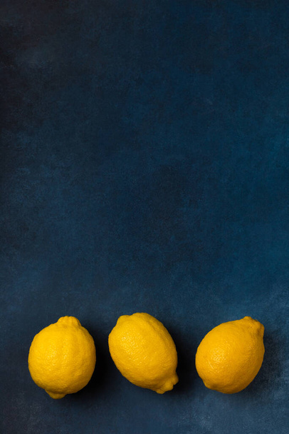 Three bright yellow citrus fruits on a blue background top view - Фото, зображення