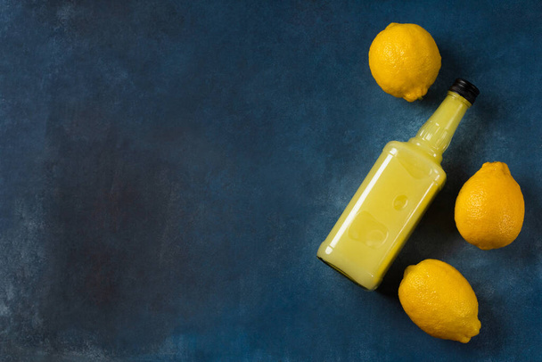 Limoncello bottle with lemons on blue background - Fotografie, Obrázek