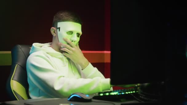 Un pirate masqué entre dans une base de données sur un ordinateur, piratant dans une pièce sombre - Séquence, vidéo