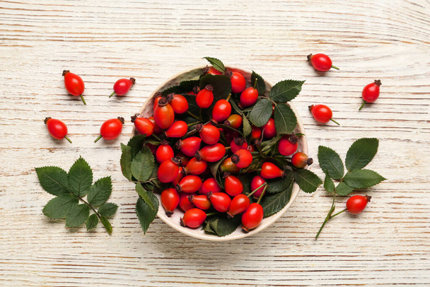 Ripe rose hip berries with green leaves on white wooden table, flat lay - Valokuva, kuva