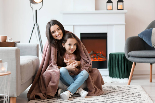 Young mother and daughter resting near fireplace at home - Foto, Imagem