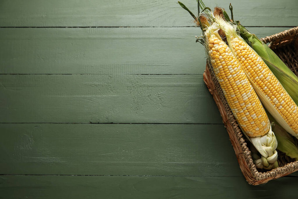 Плетений кошик зі свіжими кукурудзяними цицьками на кольоровому дерев'яному фоні
 - Фото, зображення