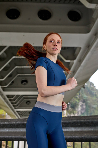 Awesome confident sports woman in stylish sportswear jogging on bridge - Fotó, kép