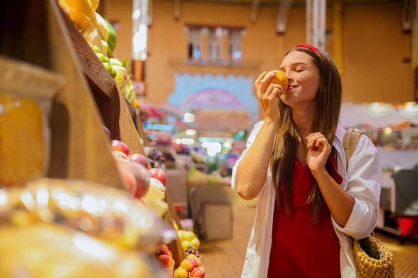 Μια γυναίκα να μυρίζει φρούτα σε ένα κατάστημα και να φαίνεται εμπλεκόμενη - Φωτογραφία, εικόνα