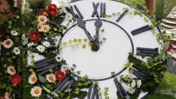 Gran reloj de pared en el campo en flores en flor, que muestra la hora 11: 55, 12: 00. concepto de gestión del tiempo, horario de verano. Primavera o boda. Picnic para mujer día - Metraje, vídeo