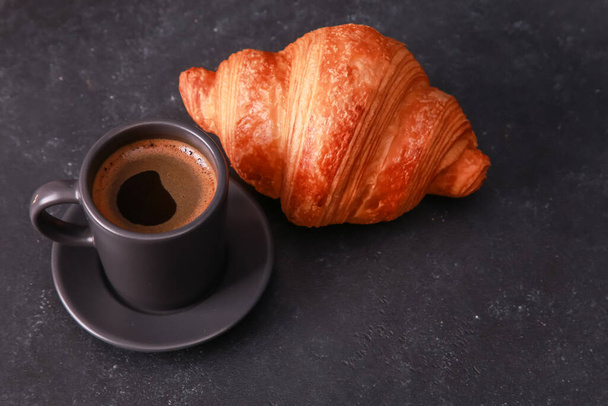 Black cup of espresso, fresh baked croissant on dark concrete table. Mug of hot coffee, bun, roll close up. Bakery food, French breakfast, morning menu, cafe concept. High angle, copy space - Фото, изображение