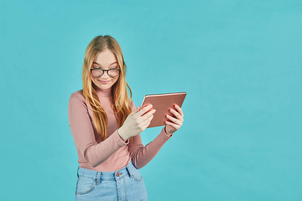 Smart looking girl with glasses. Social media and online communication. Attractive young student with digital tablet isolated on blue background. - 写真・画像