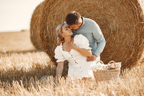Happy couple sitting on bale in farmland - Foto, Imagen