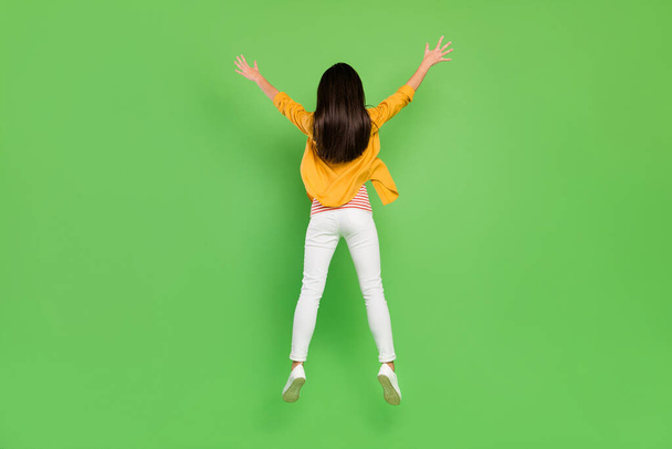 Pieno corpo indietro foto di funky marrone acconciatura giovane signora salto indossare pantaloni camicia scarpe da ginnastica isolato su sfondo di colore verde - Foto, immagini