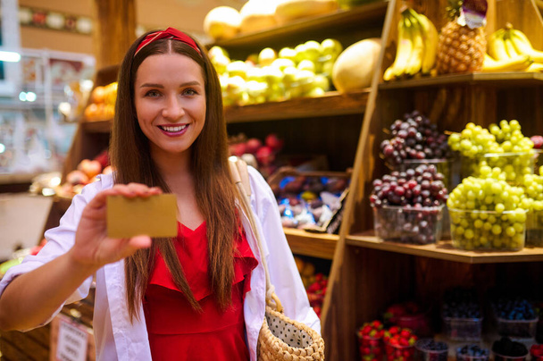 Eine Frau hält eine Kreditkarte in der Hand, während sie in einem Geschäft für Obst bezahlt - Foto, Bild
