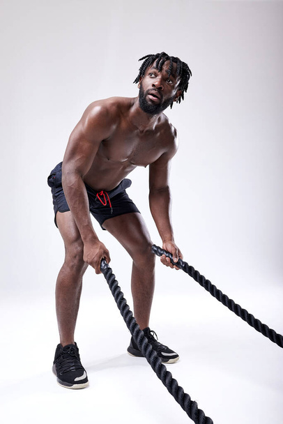Young muscular african man working out with heavy ropes. Isolated on white - Fotografie, Obrázek