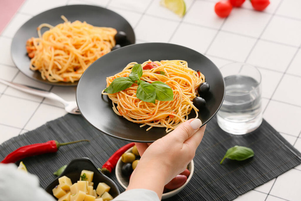 Woman holding plate with tasty Pasta Puttanesca at table in restaurant - Φωτογραφία, εικόνα