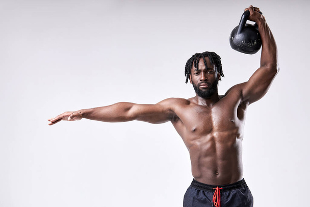 Muscular sportsman, shirtless guy lifting up kettlebell isolated on white studio background. - Photo, image