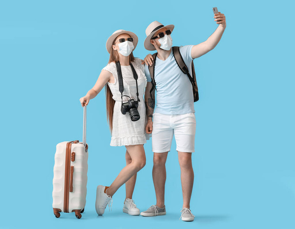 Couple of tourists in medical masks taking selfie on color background - 写真・画像