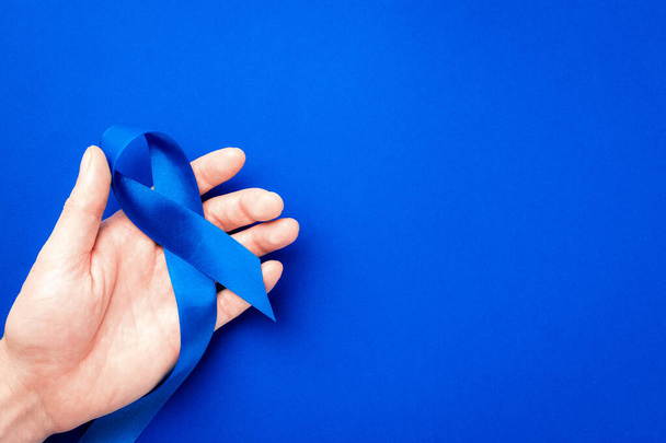 Männer Krebs. Blaues Band in den Händen isoliert auf tiefblauem Hintergrund. Bewusstsein Prostatakrebs bei Männern Gesundheit im November. Konzept des Adrenokortikalen Karzinoms - Foto, Bild