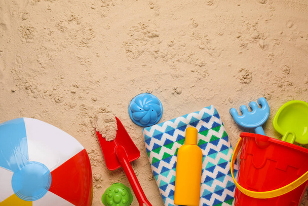 Colorful inflatable ball, plastic beach toys, sunscreen and blanket on sand, flat lay. Space for text - Photo, image