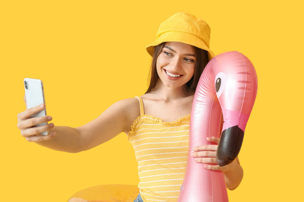 Young woman with inflatable ring taking selfie on color background - 写真・画像