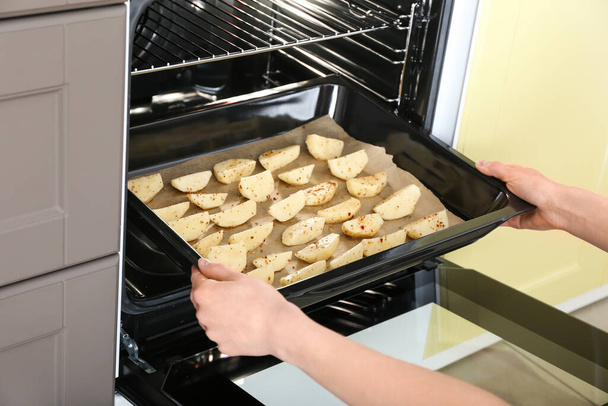 Vrouw zet dienblad met aardappel in de oven - Foto, afbeelding