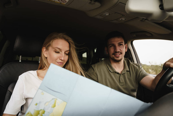 Young loving couple on a road trip using map inside a car - Fotó, kép