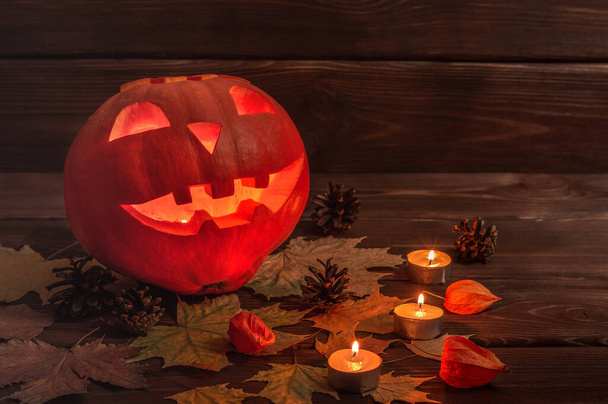 Halloween. Jack lucerna z dýně, hořící svíčky a spadlé listí a kornouty na tmavém dřevěném pozadí. - Fotografie, Obrázek