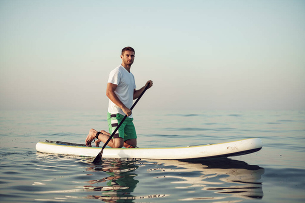 Young man in t-shirt and shorts floating on SUP board - Fotoğraf, Görsel