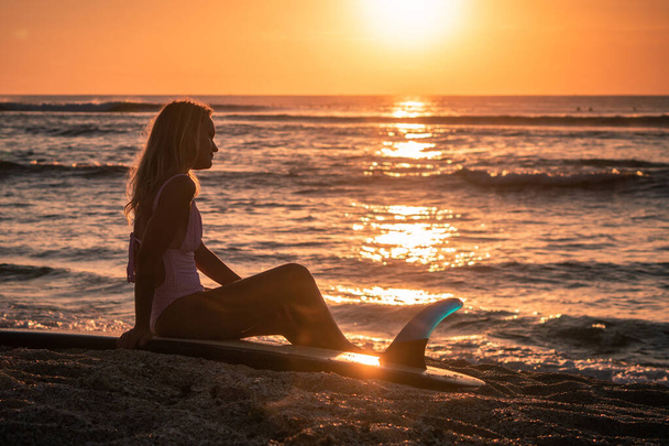 Portrait of young blonde surfer girl with white long surf board single fin on the beach at sunset time in Bali - Foto, afbeelding