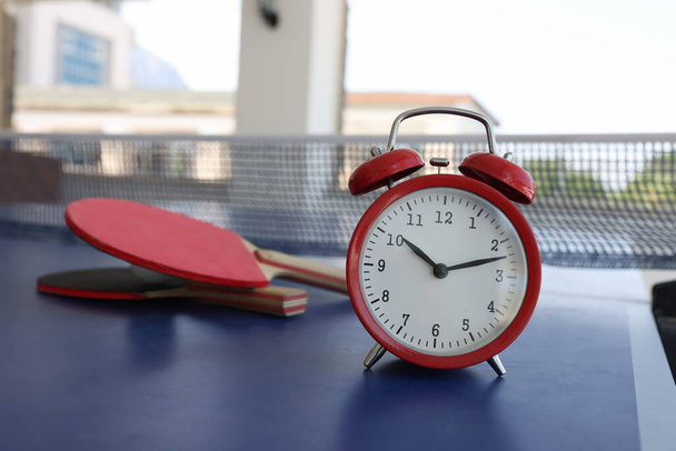 Relógio de alarme vermelho em pé na mesa de tênis perto raquetes close-up - Foto, Imagem