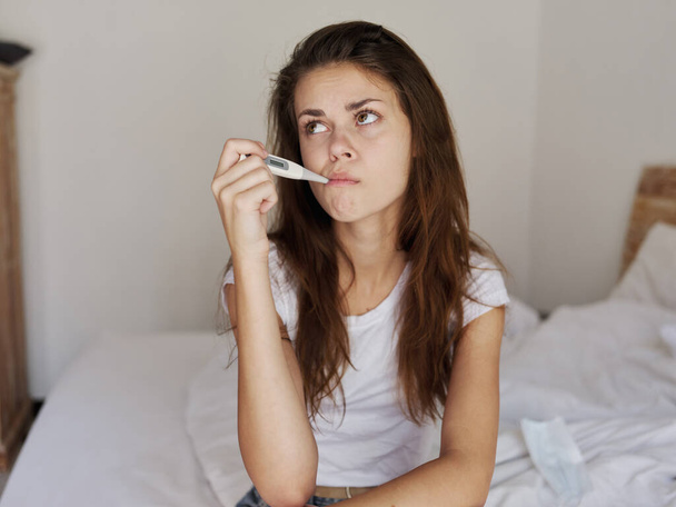 woman waiting with a thermometer in her mouth sitting on the bed - Foto, Bild