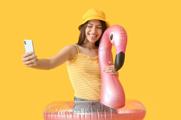 Νεαρή γυναίκα με φουσκωτό δαχτυλίδι που παίρνει selfie στο φόντο χρώμα - Φωτογραφία, εικόνα